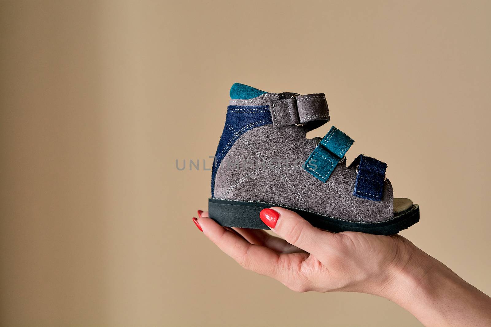 Female is holding close-up a special children's orthopedic shoe sandals made of genuine leather. Comfortable shoes isolated on light background with copyspace. Image suitable for advertising.