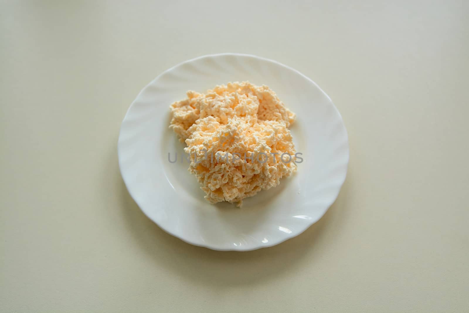 Shredded Cream Cheese on a white plate on a light background in daylight. Grated melted cheese.