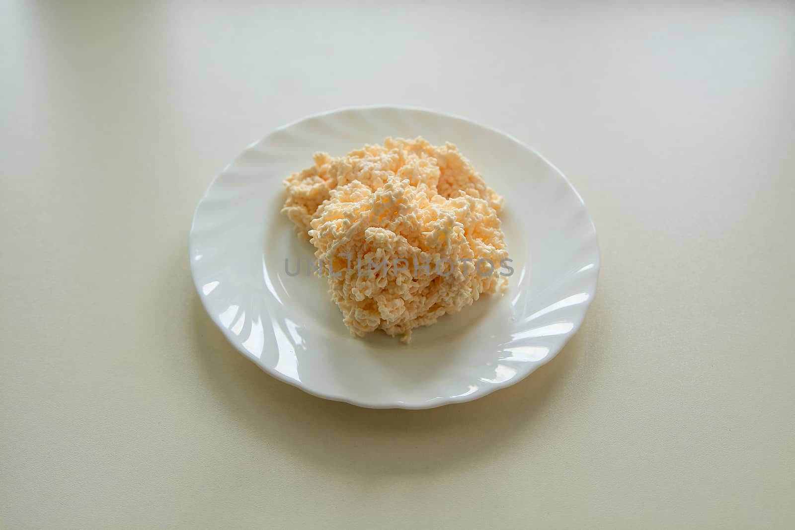 Shredded Cream Cheese on a white plate on a light background in daylight. Grated melted cheese.