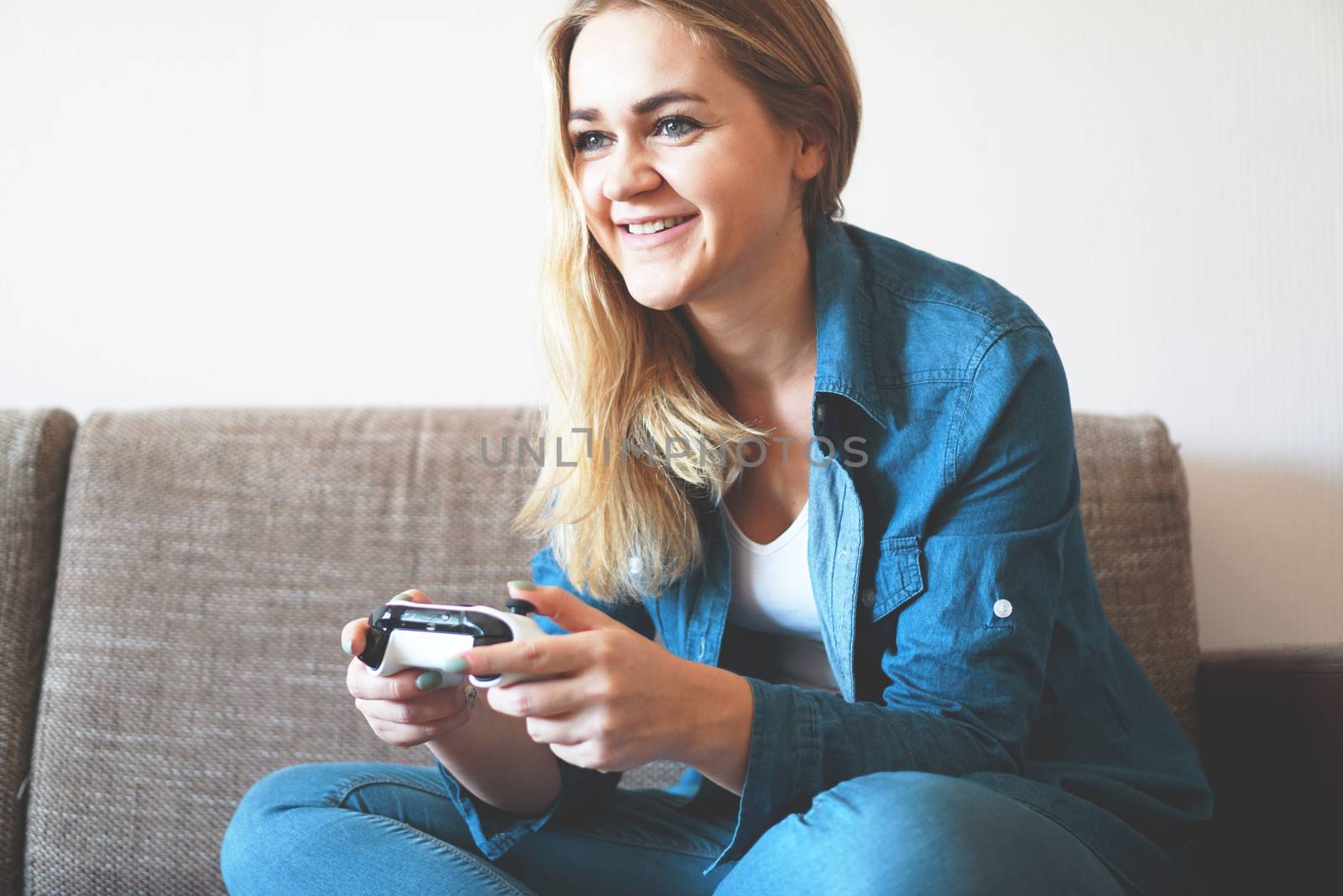 Girl gamer plays with a wireless gamepad while looking at the screen in front of her. Young blonde girl smiles and enjoys playing video games console.