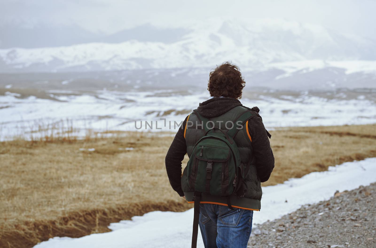 Man wearing backpack and looking at the winter mountains by Novic