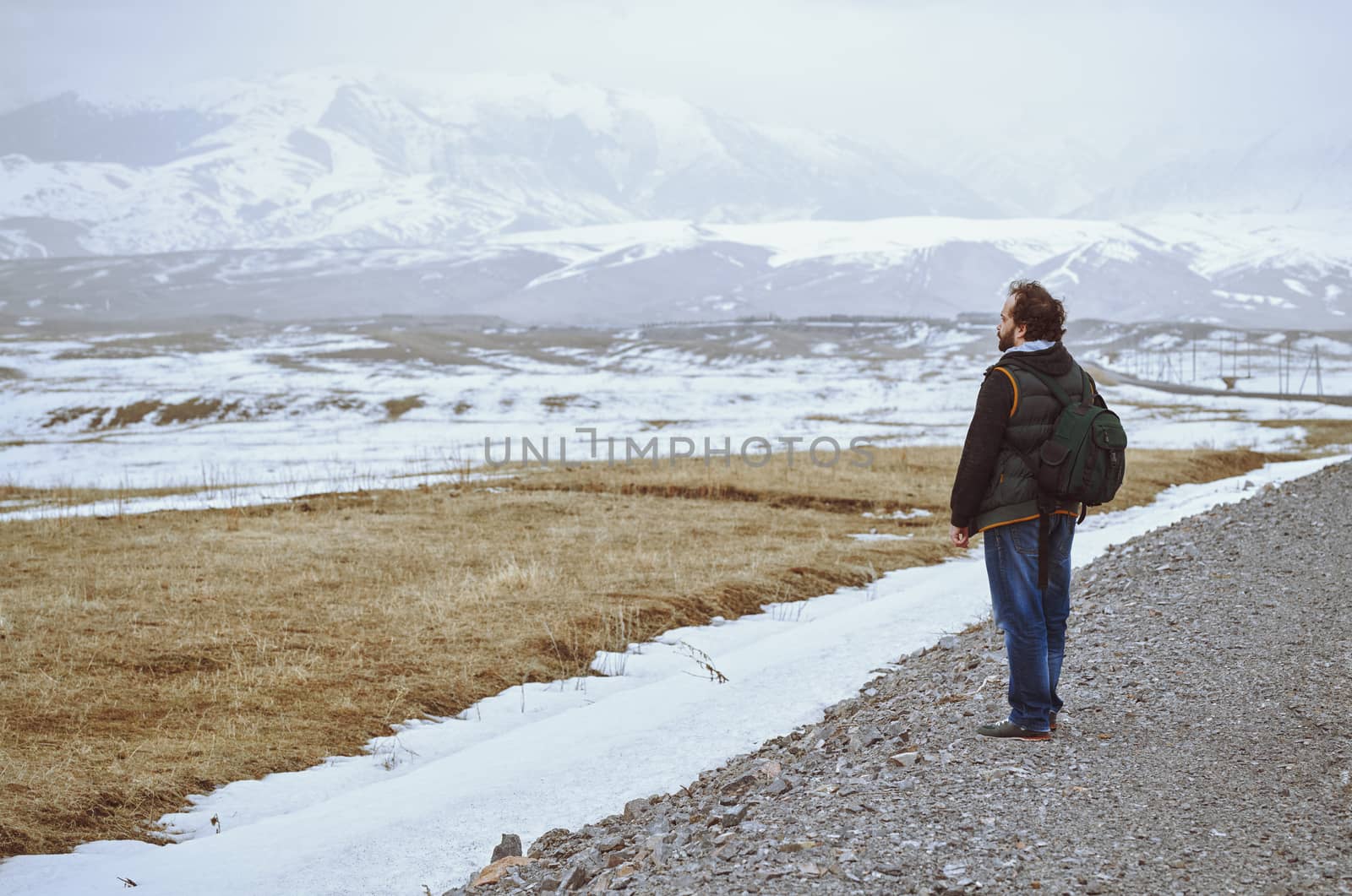 Touris wearing backpack and standing at the rural road while looking at the winter mountains