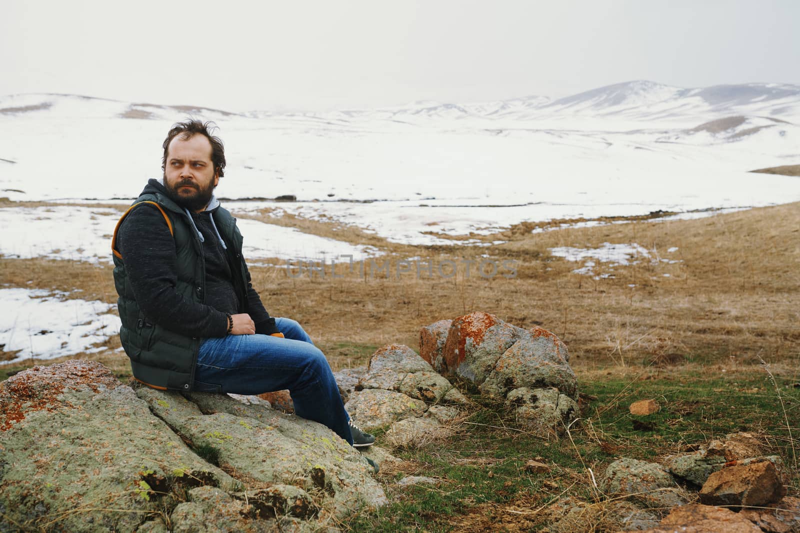 Man sitting on the stones and looking at winter nature view