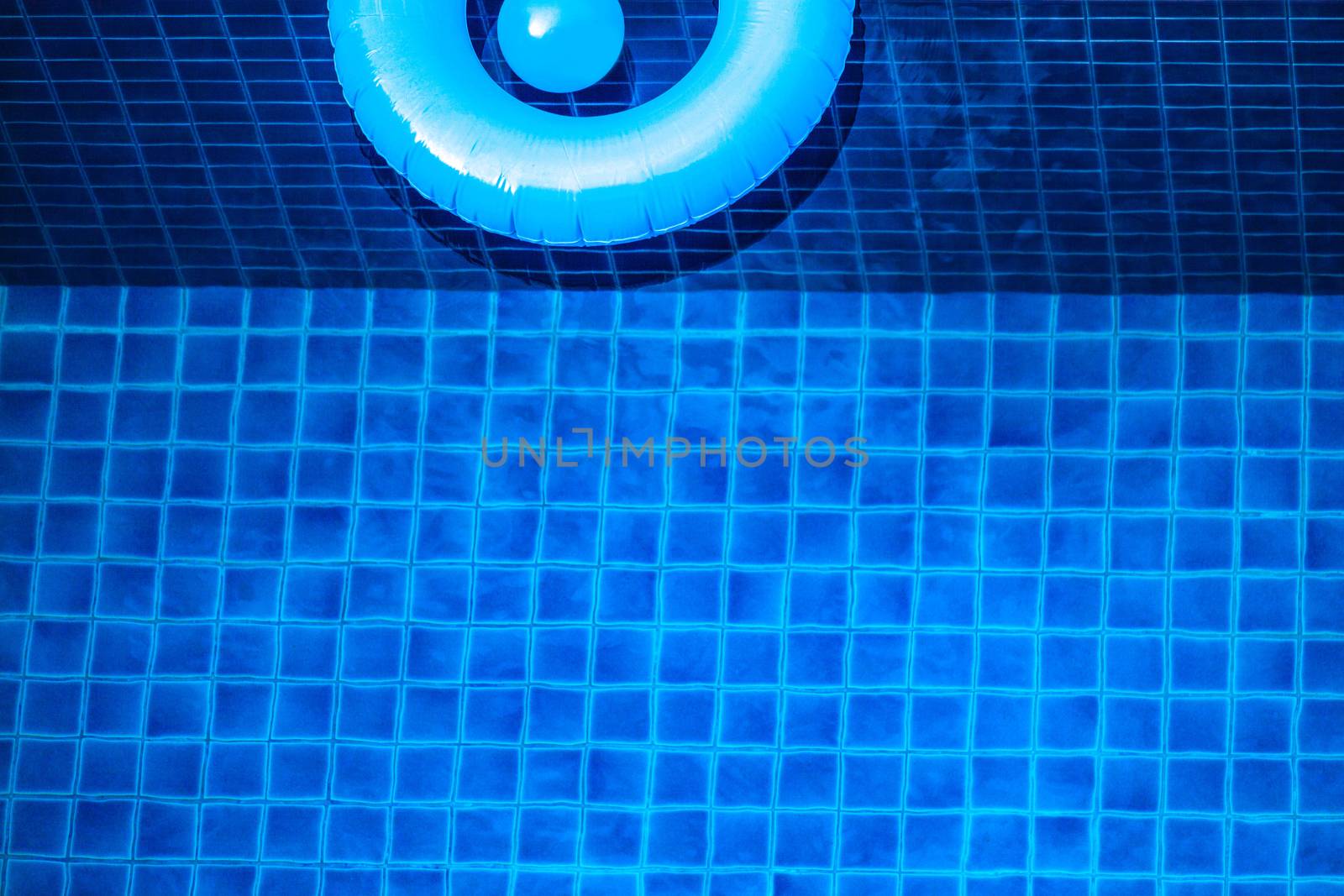 Aerial view of inflatable ring toy in swimming pool water from above, vacation concept background