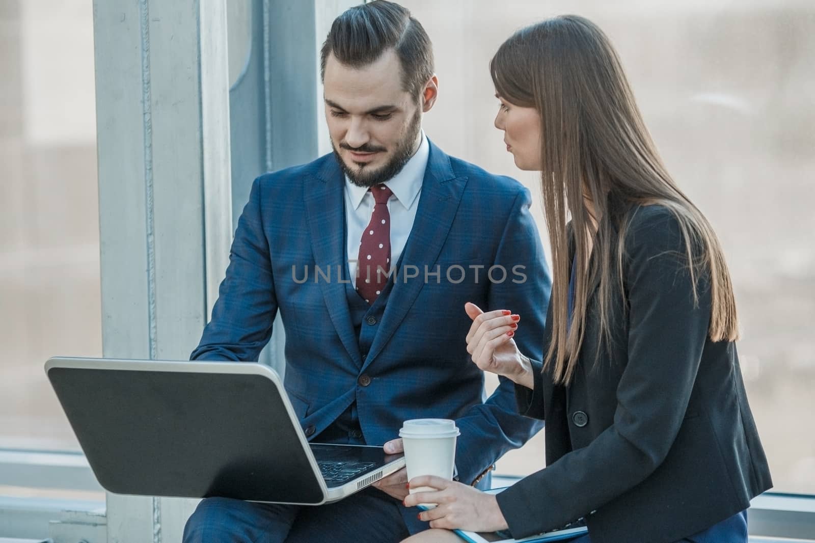 Cheerful office workers discussing their project at laptop over cup of coffee