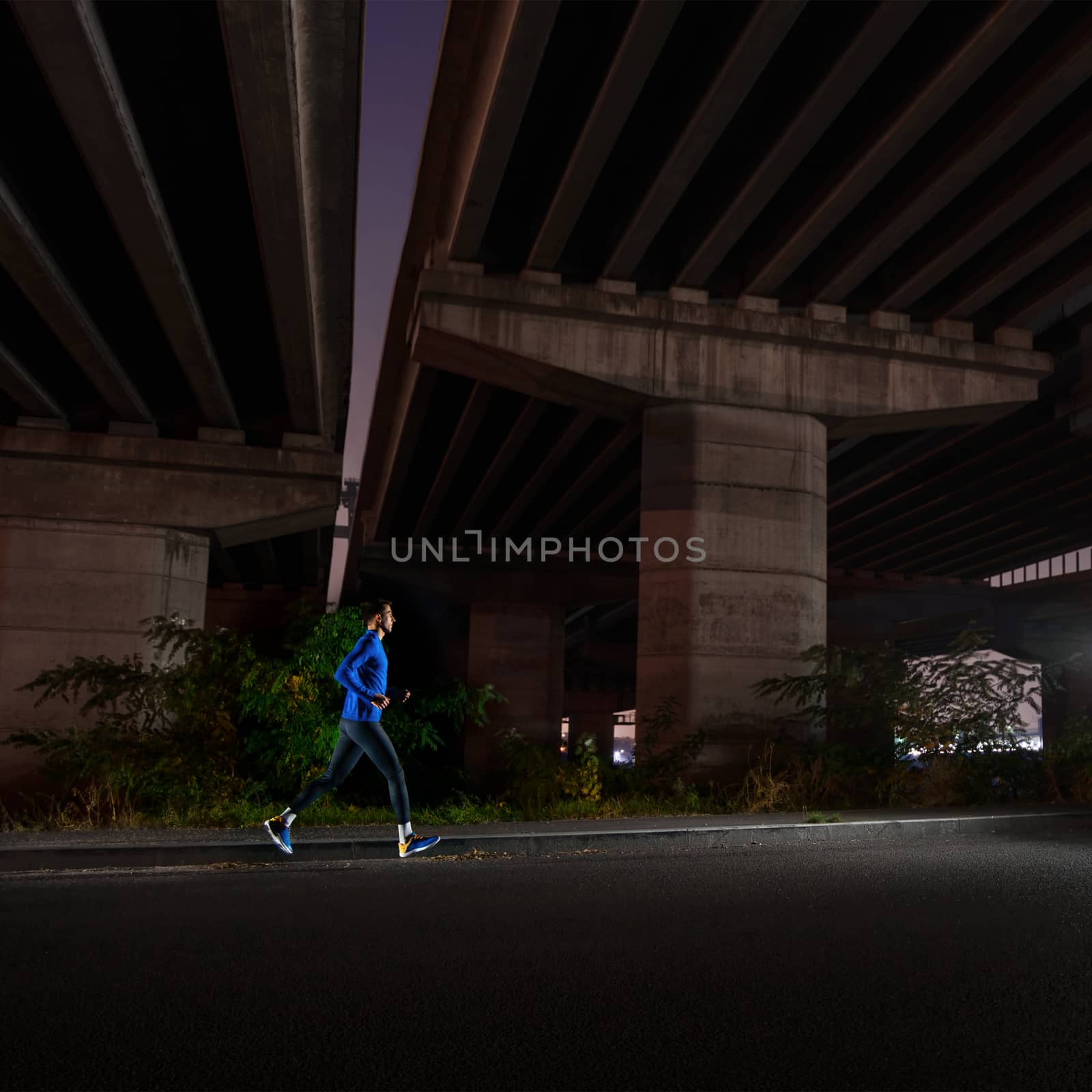 Young Man in Blue Running at Night. Urban Running. Healthy Lifestyle and Sport Concept. by maxpro