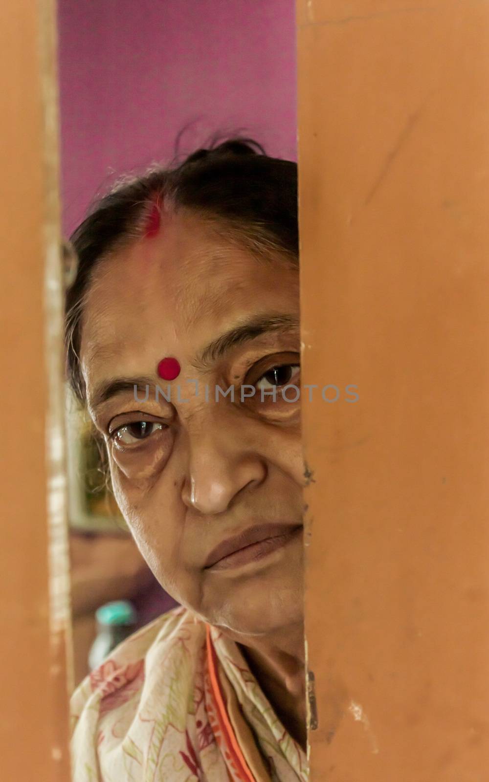 Thoughtful, sad, Worried and alone elderly senior woman peeping through the door at home and eagerly waiting for her son to come. Loneliness concept