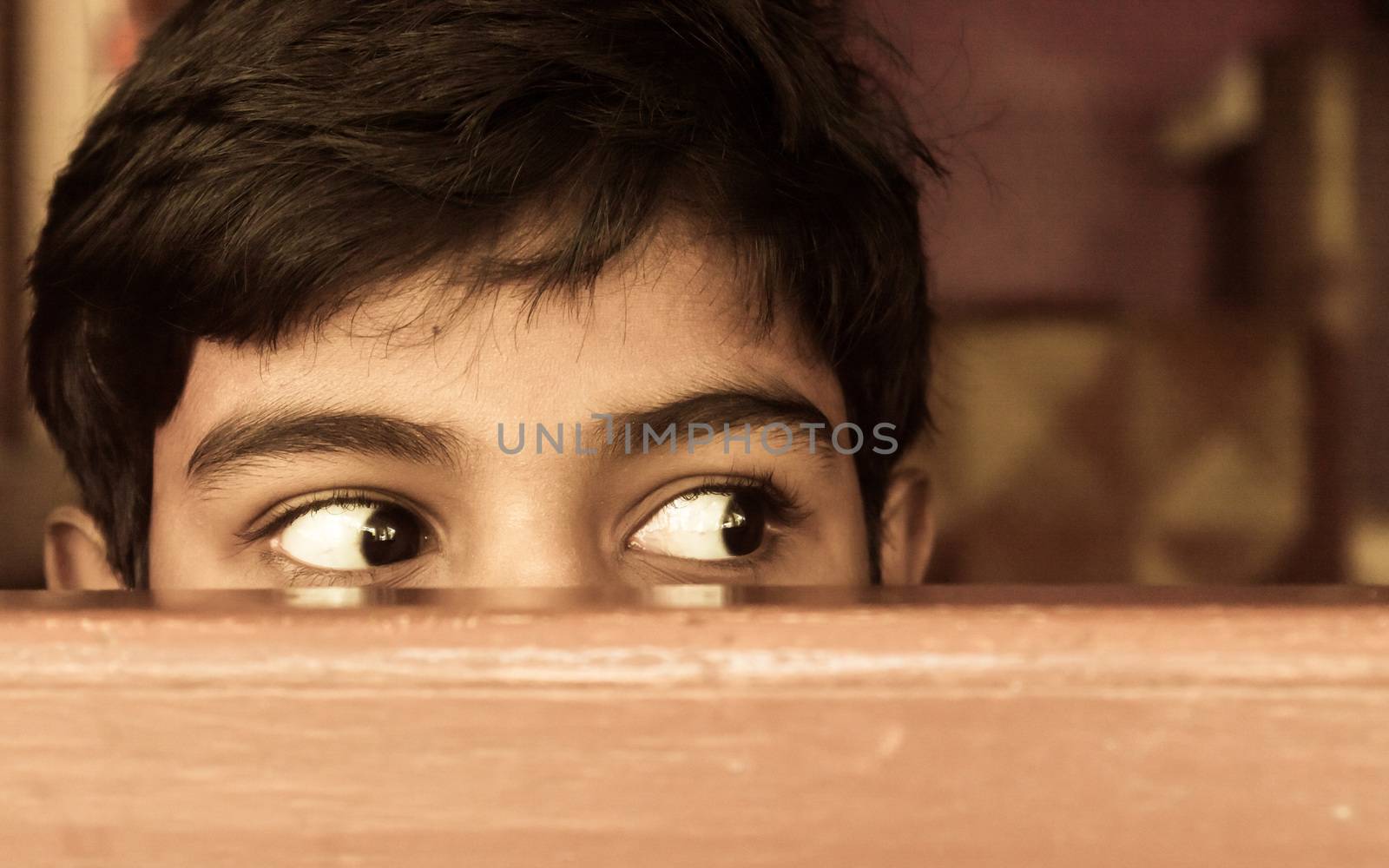 Young boy curiously looking outside through a window. by sudiptabhowmick