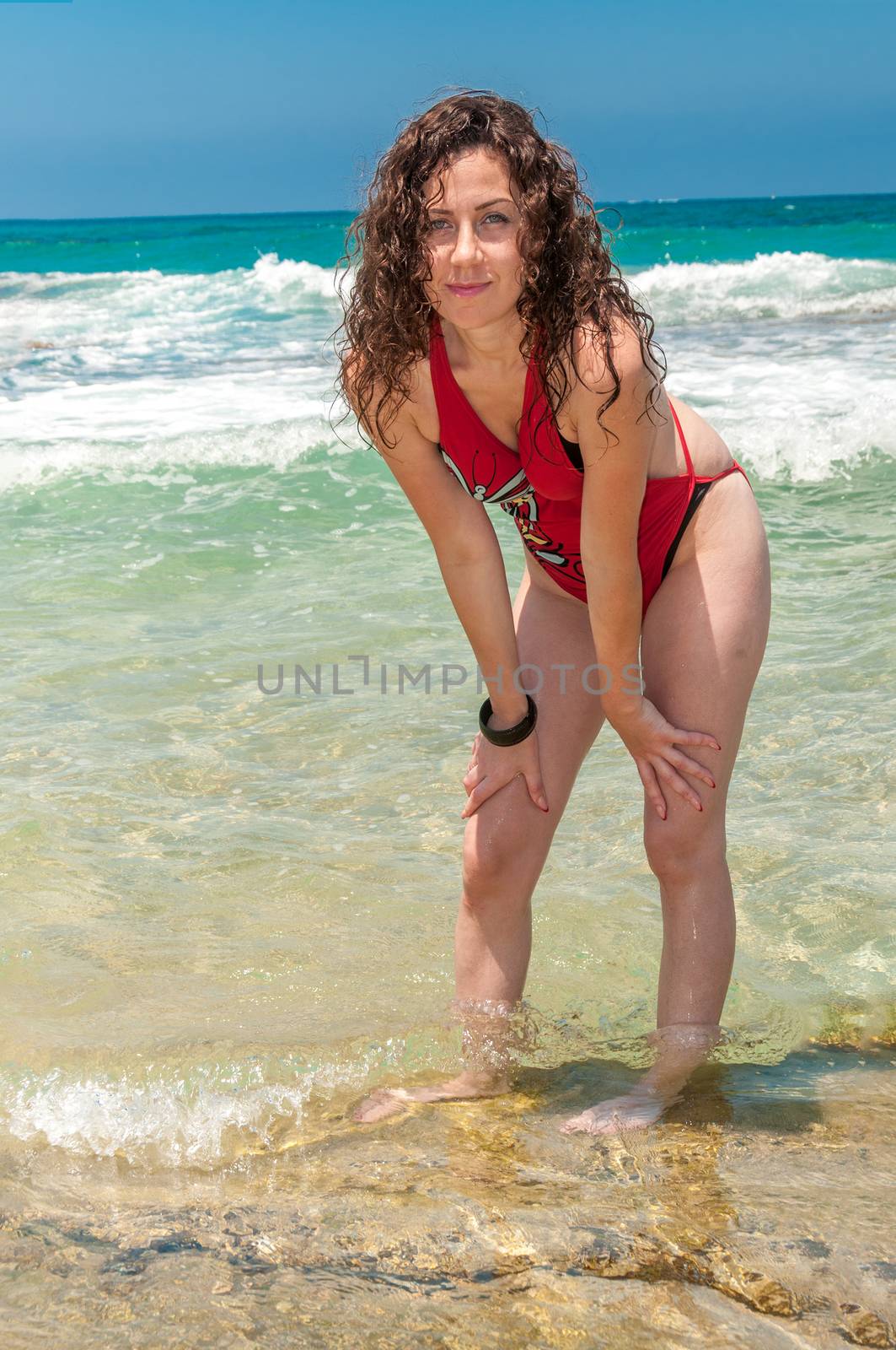 The girl, with her hair down, fooling around and teasing the photographer, standing in the sea in a beautiful, red bathing suit