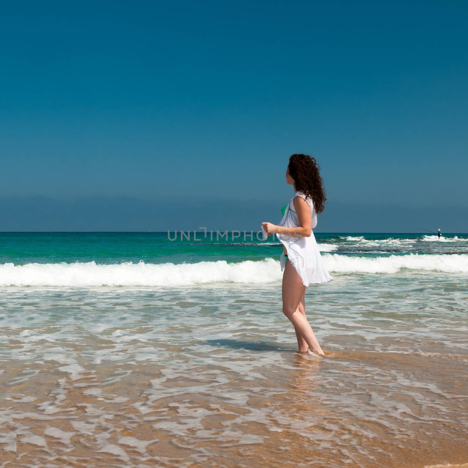 A model in a green bikini and white, translucent cape is photographed on the sea beach