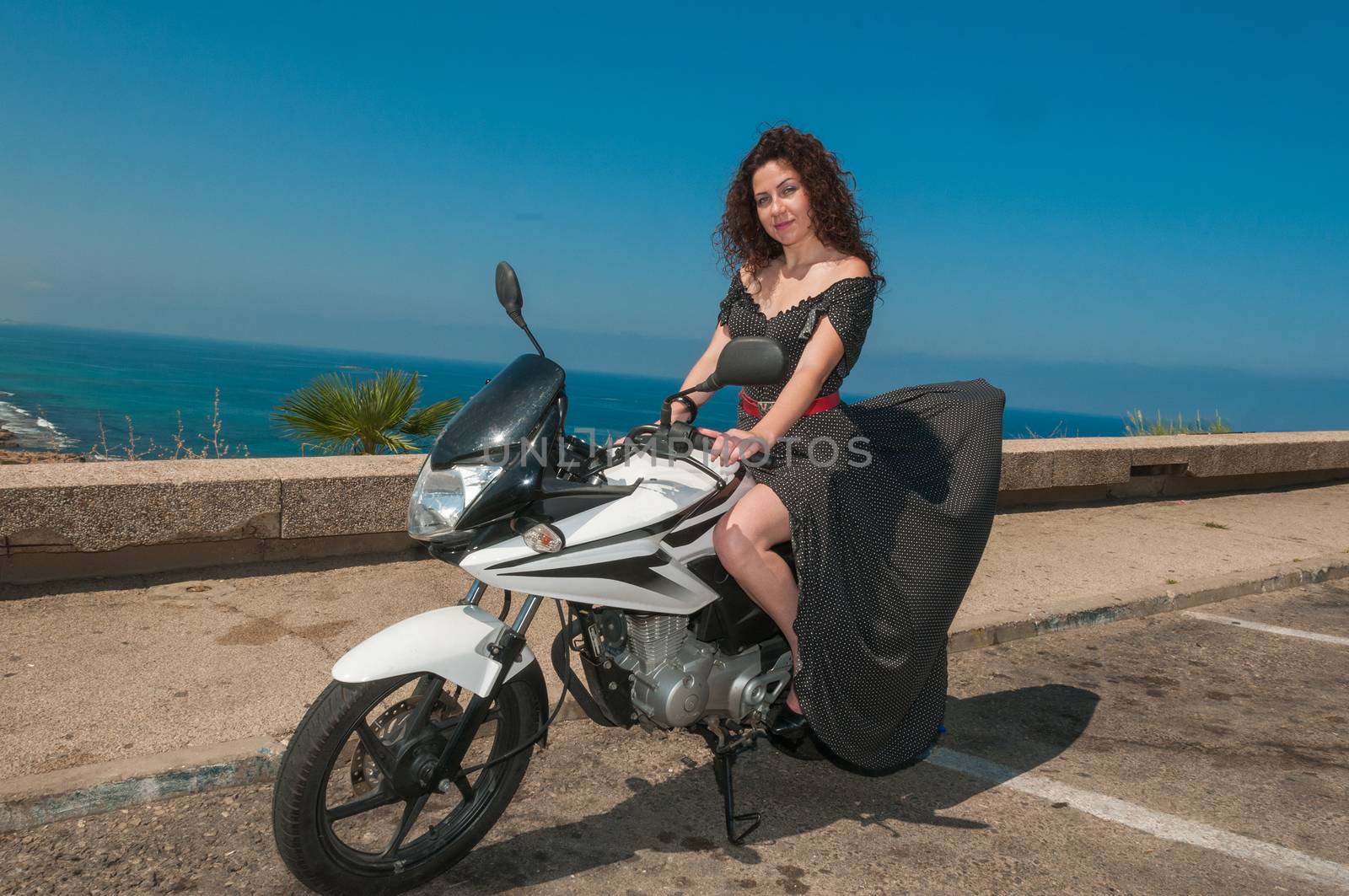 Photo of a young girl-model sitting on a sports bike, against the sea