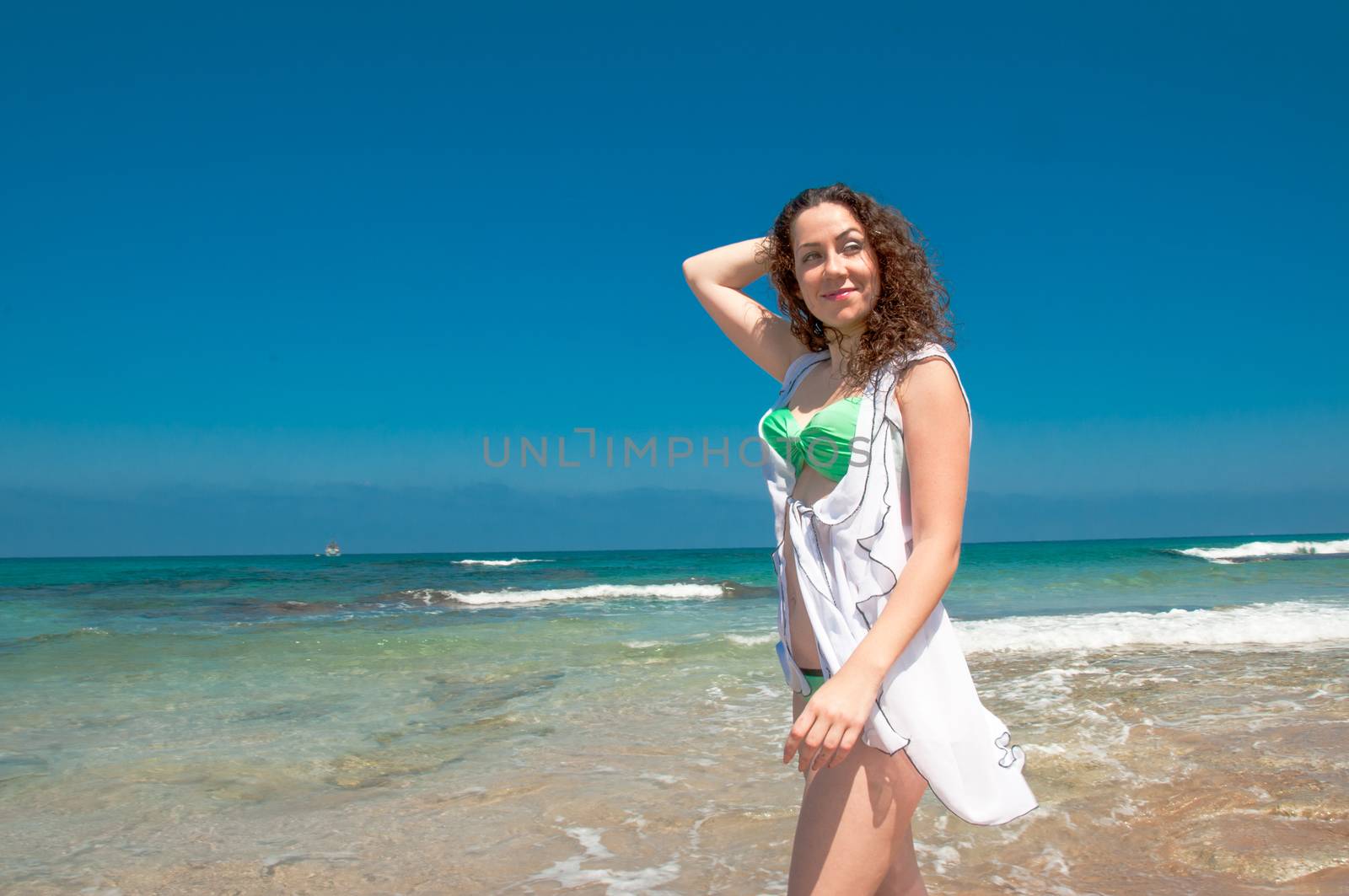 A model in a green bikini and white, translucent cape is photographed on the sea beach