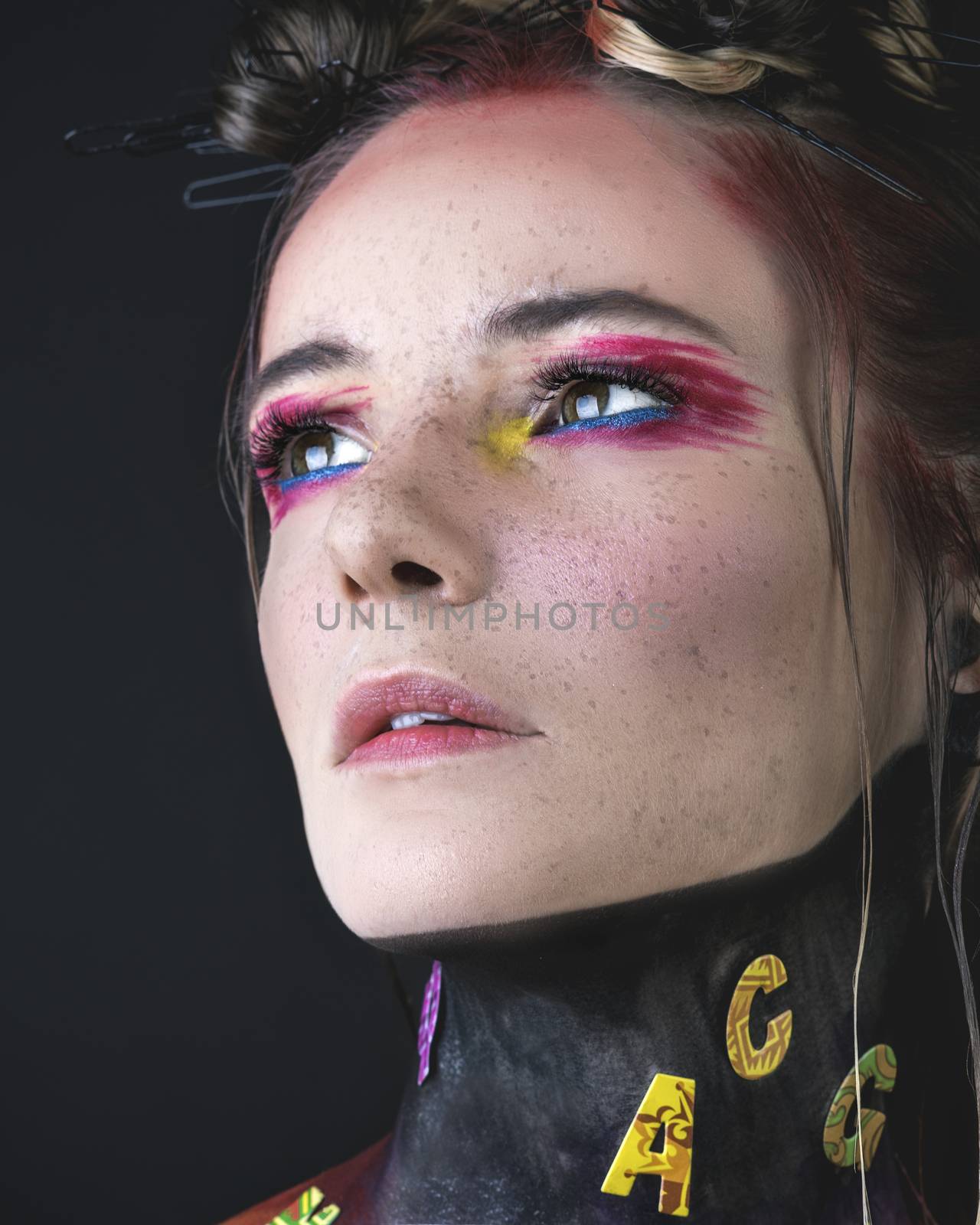 Emotional portrait of a young girl with creative makeup and colorful letters on her shoulders
