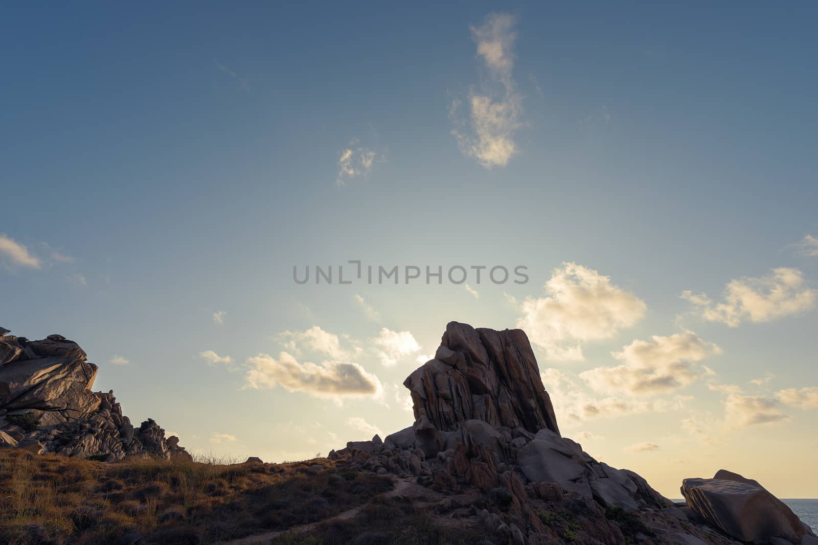 rocky nature landscape by the coast, the sunset sun shines in the clear sky with few clouds and illuminates some rocks and bushes, Copy space, Capo Testa, Santa Teresa di Gallura, Sardinia, Italy