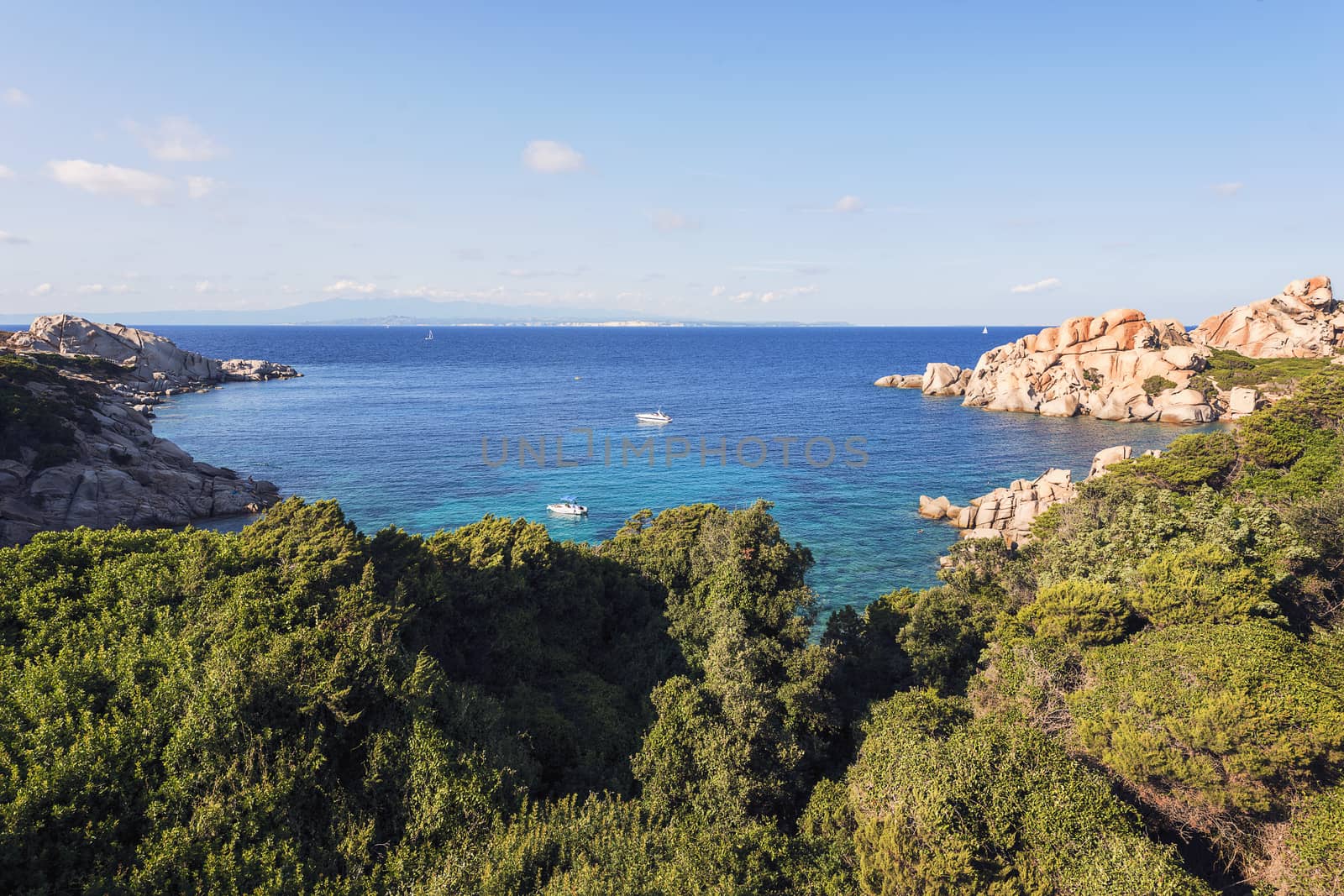 panoramic view of a cove with anchored boats. Vegetation and rocks surround it, scenic place for vacationers and summer holidays, bright colors. Capo Testa, Santa Teresa di Gallura, Sardinia, Italy