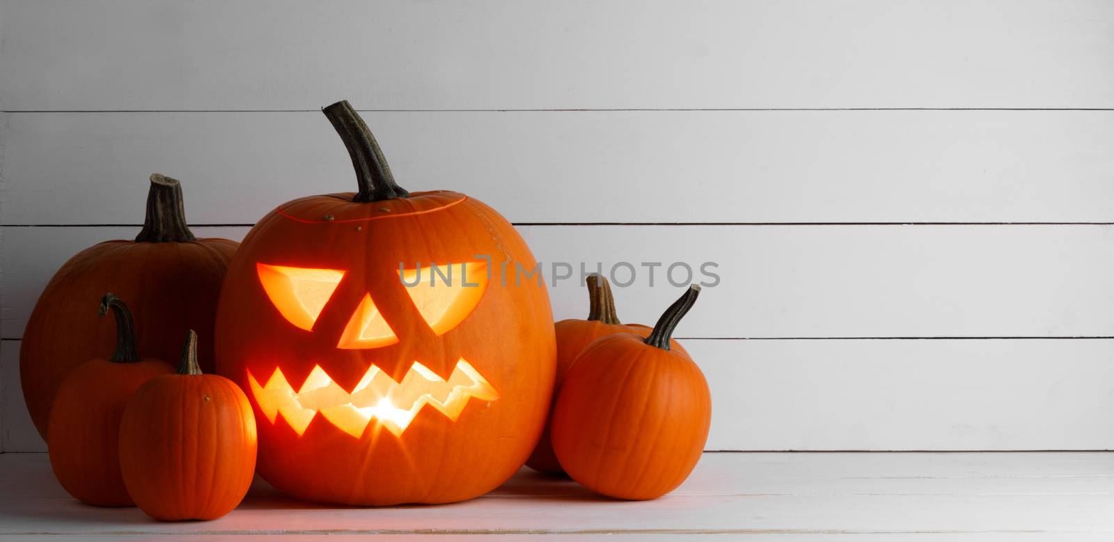 Glowing Halloween pumpkin heads jack o lantern on white wooden background with copy space for text
