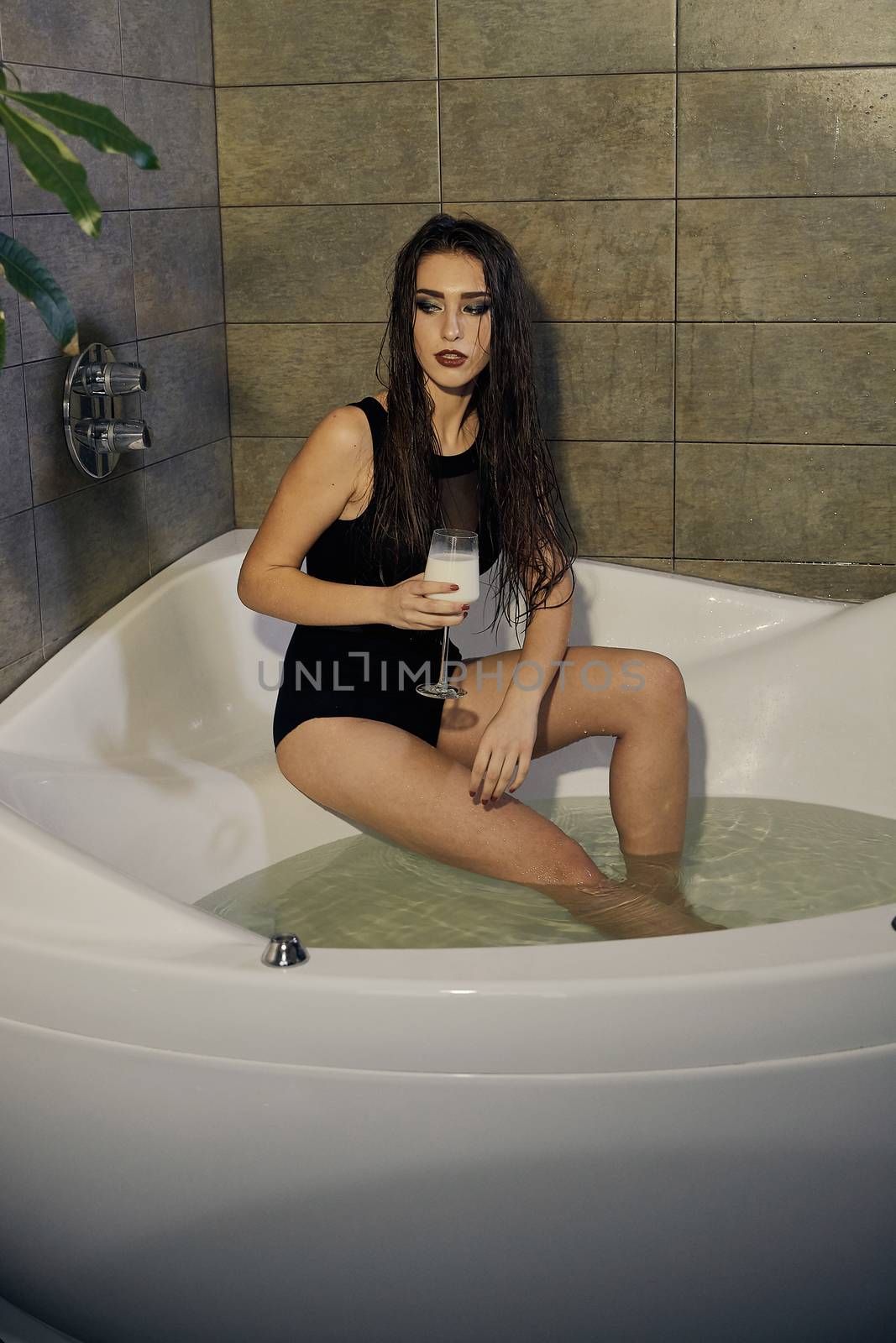 Girl in a black bathing suit holding a glass of milk in the bathroom. Conceptual fashion photography for design. Skin care and a healthy lifestyle. Closeup naked girl. Sexy woman portrait.