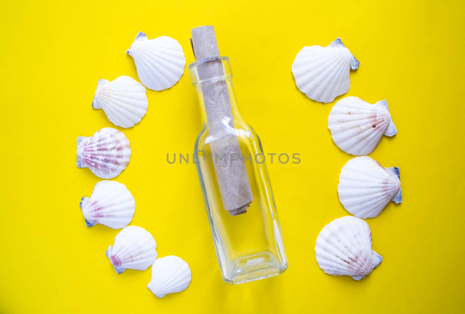 Semicircle of white seashells with message in a glass bottle on yellow background