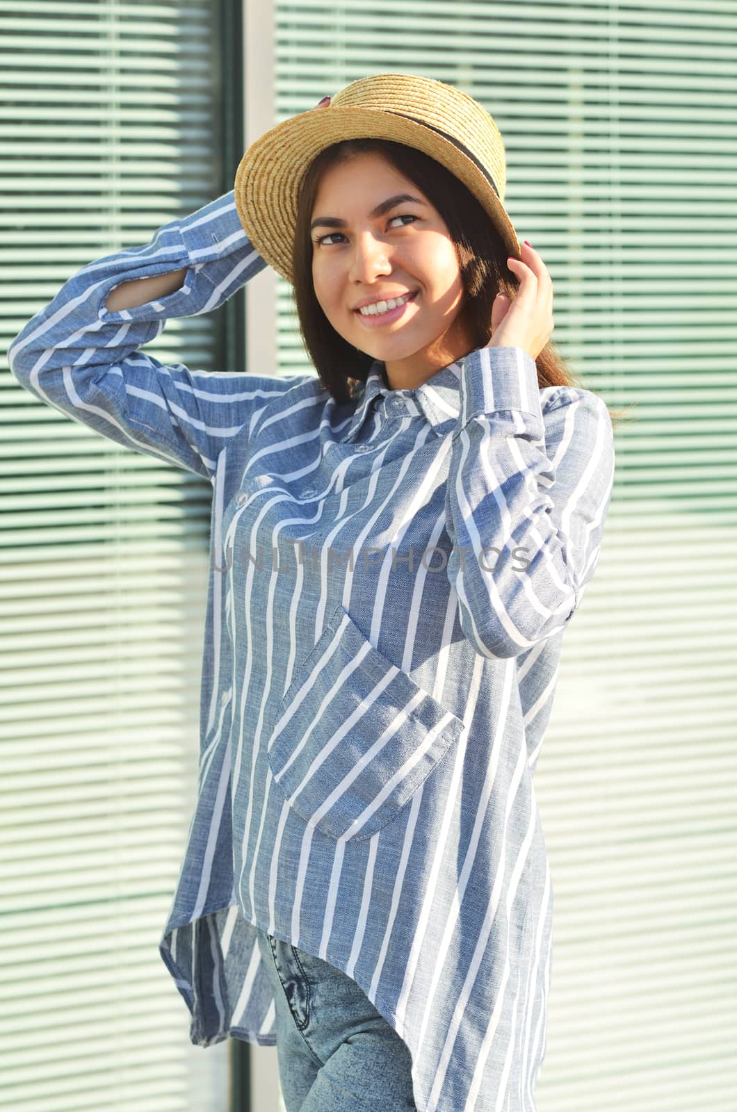 Portrait of a young girl is standing near the wall in a hat, and she is dressed in blue striped shirt by xzgorik