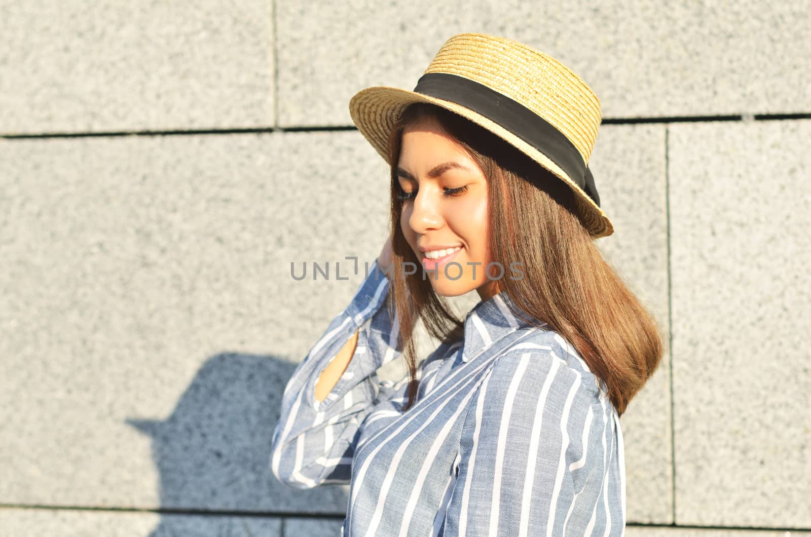 Portrait of a young girl is standing near the wall in a hat, and she is dressed in blue striped shirt