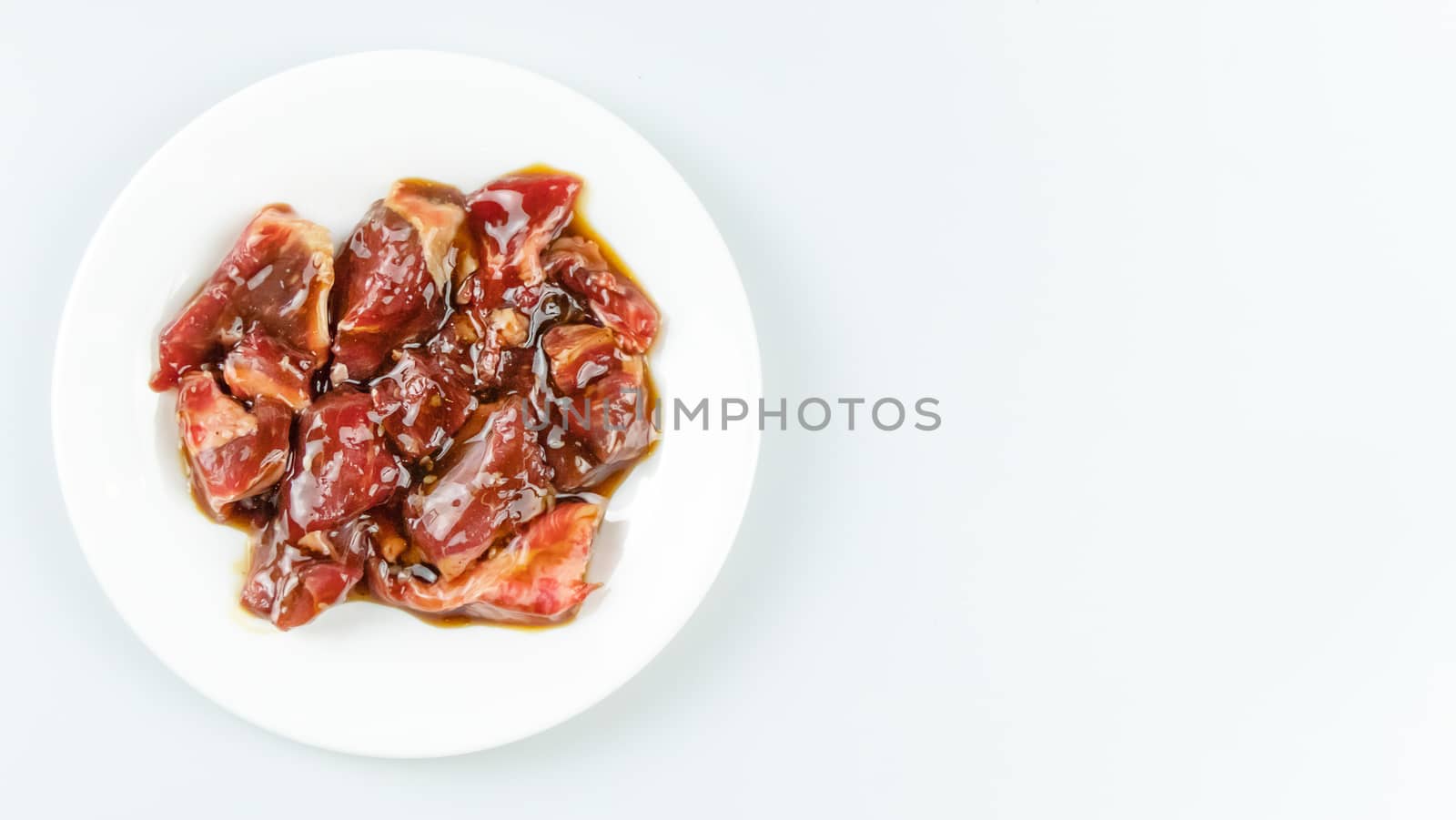 Top view of some raw beef with sauce on a plate over white background