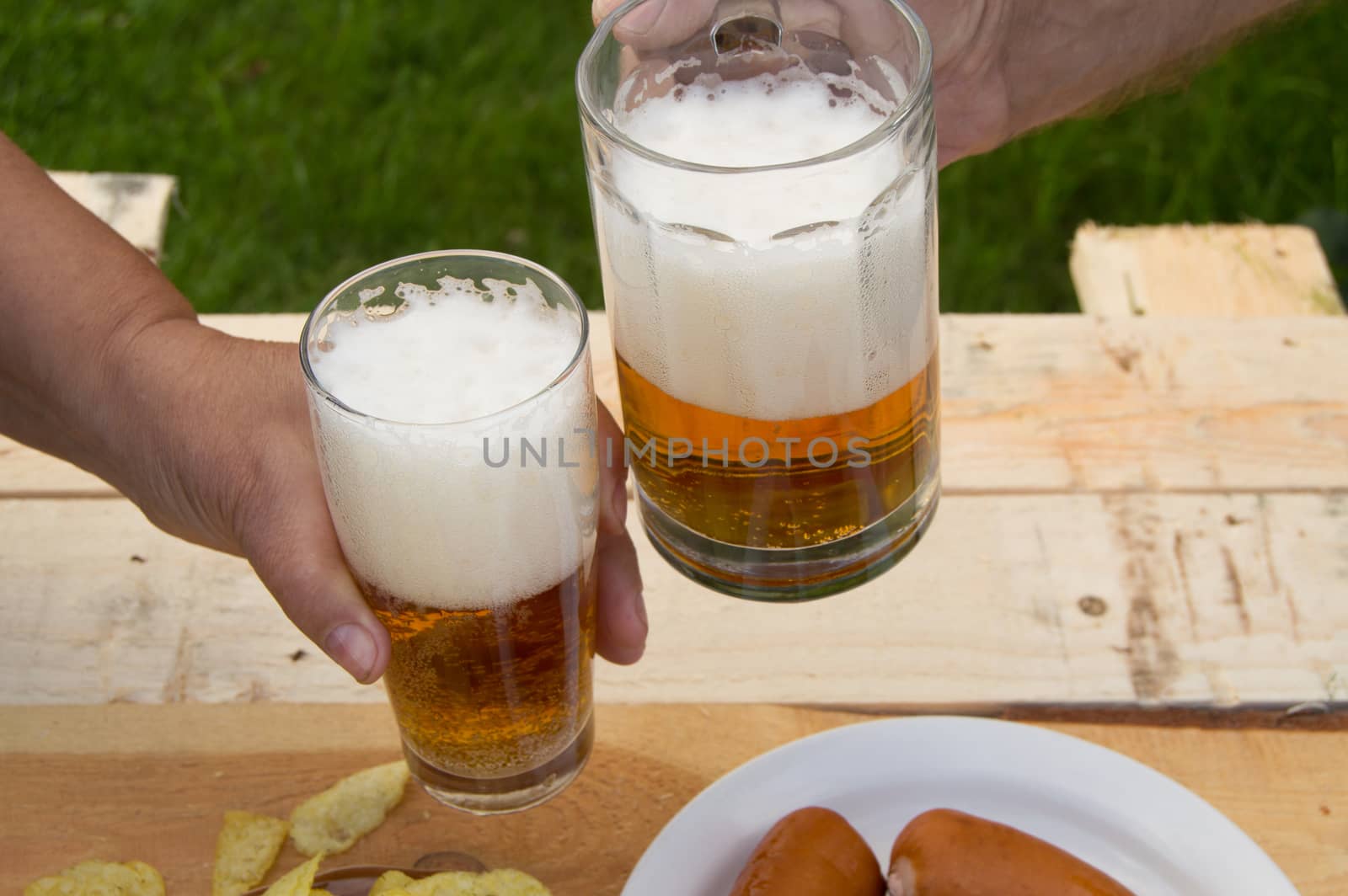 hands holding glasses with beer, chips and sausages lying on a light wooden boards, people relax in the weekends, Octoberfest by claire_lucia