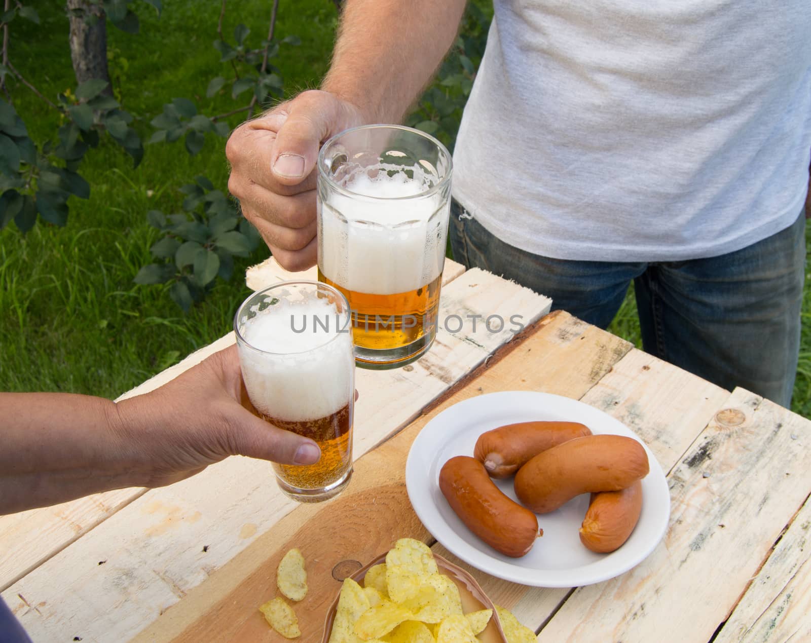 hands holding glasses with beer, chips and sausages lying on a light wooden boards, people relax in the weekends, Octoberfest by claire_lucia