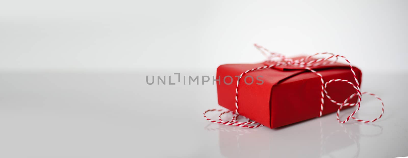 Christmas gift box wrapped in red paper and bow of dtriped rope on white background