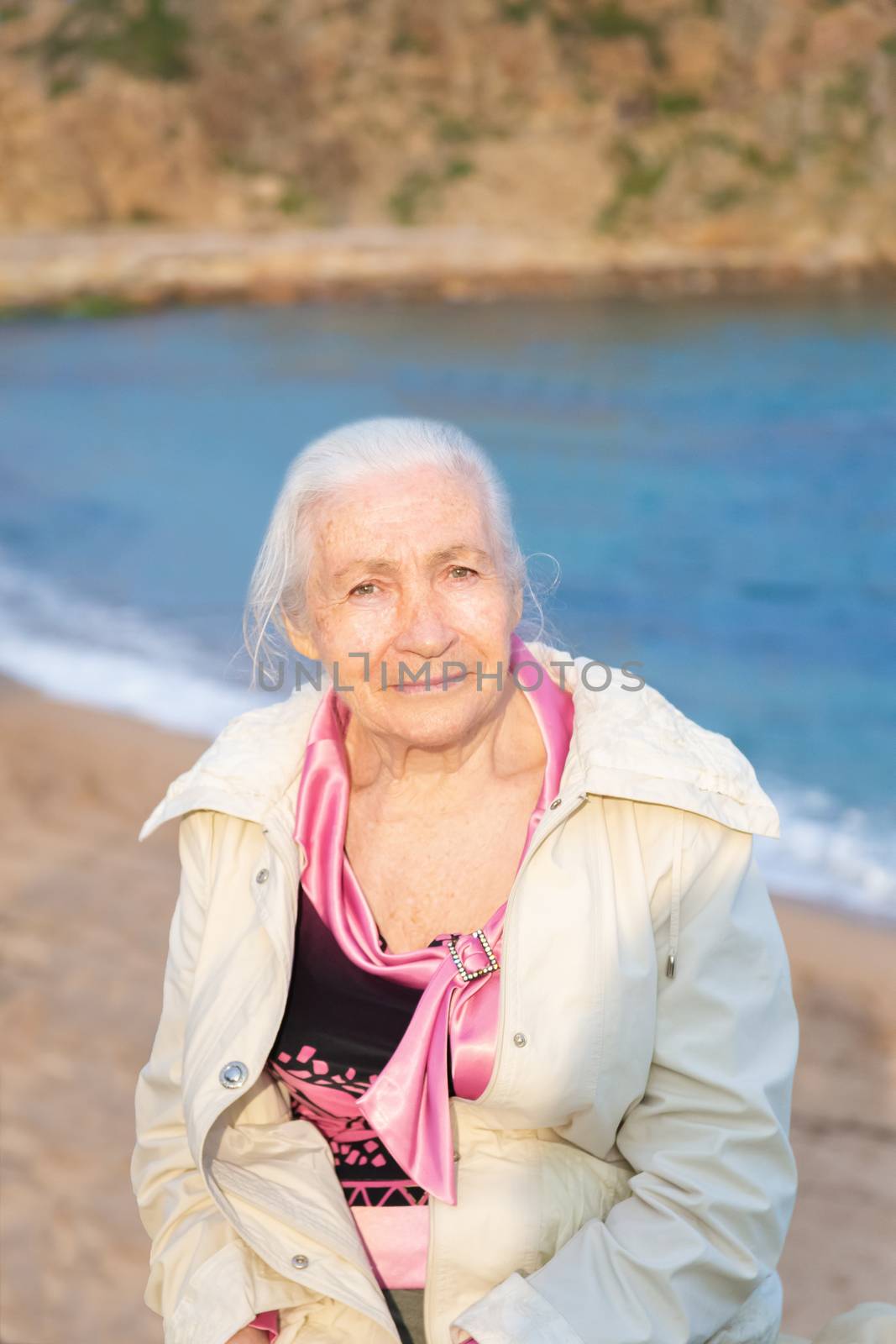 Portrait of the happy elderly woman against the sea in sunny spring day.