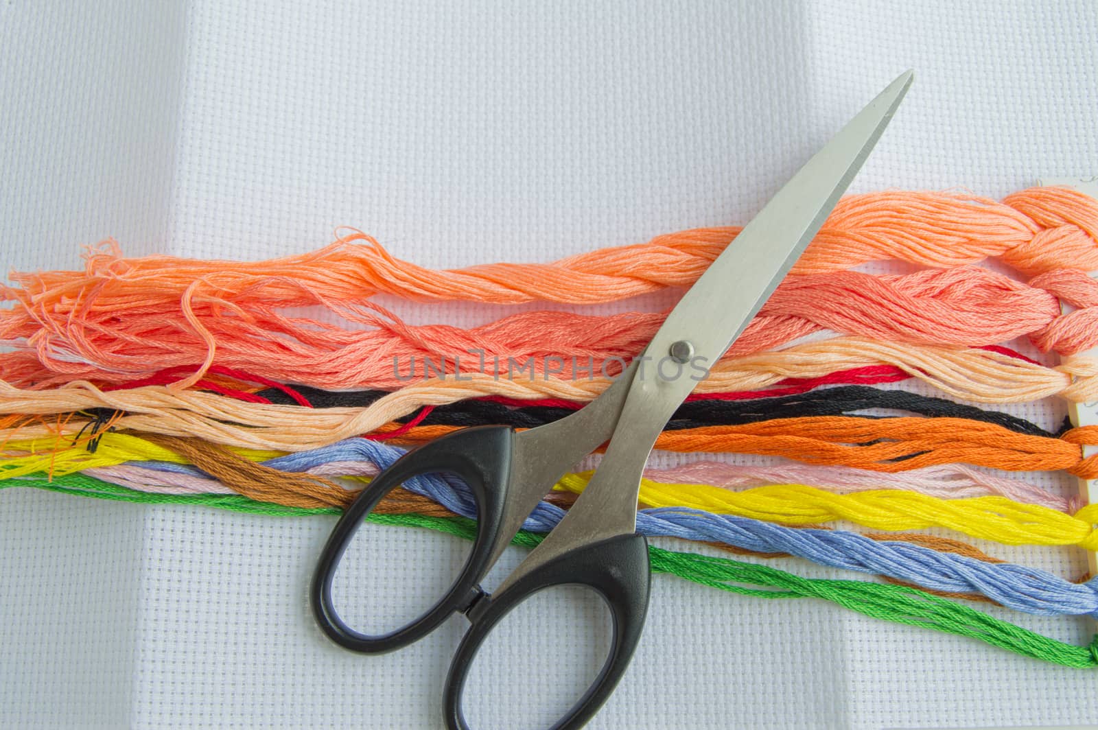 Scissors and bright colorful thread for embroidery thread on canvas. Handmade accessories on white background. Place for text, top view.