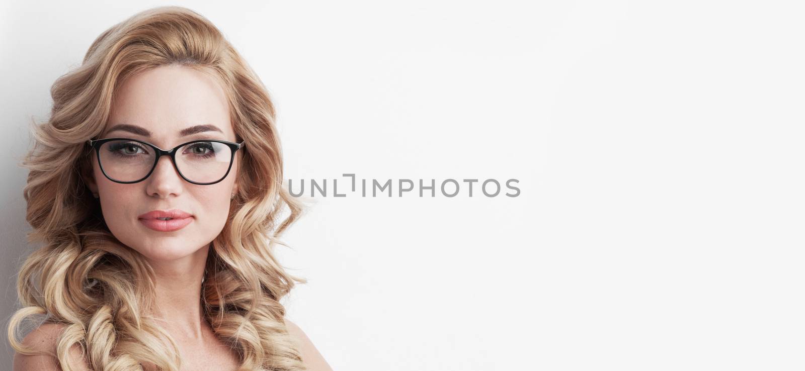 Portrait of beautiful caucasian blonde woman with curly hair standing on white background. Young business woman with glasses looking at camera