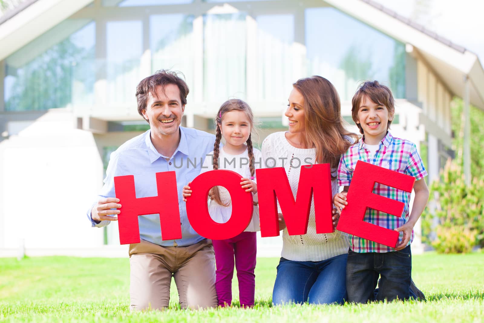 Happy family of parents and children in front of their house outdoors holding HOME letters