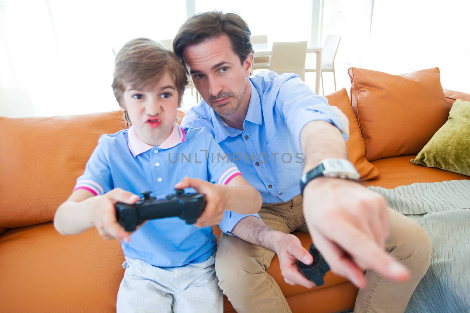 Father and son sitting on sofa in lounge playing video game