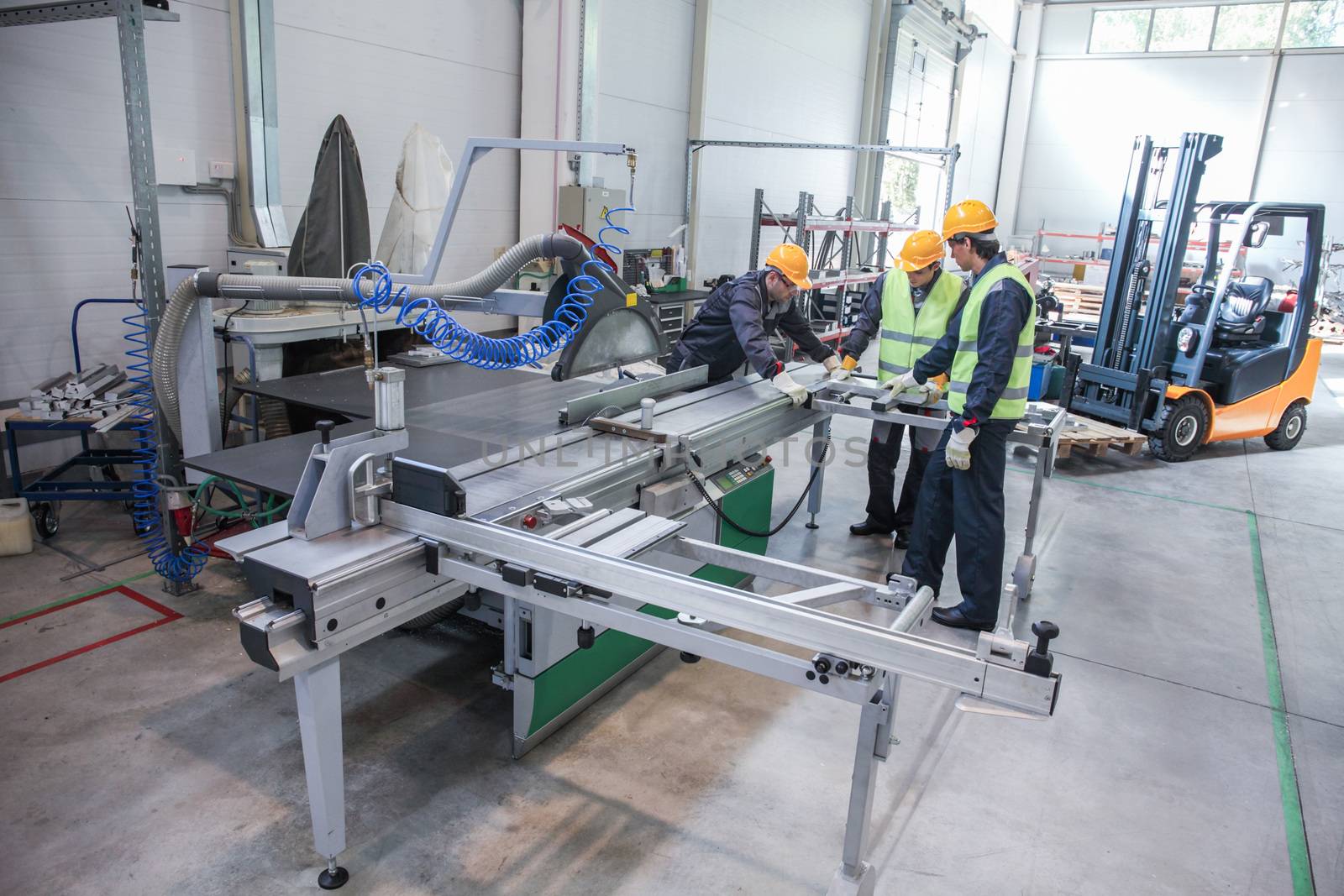 Team of three workers in CNC factory working at machine