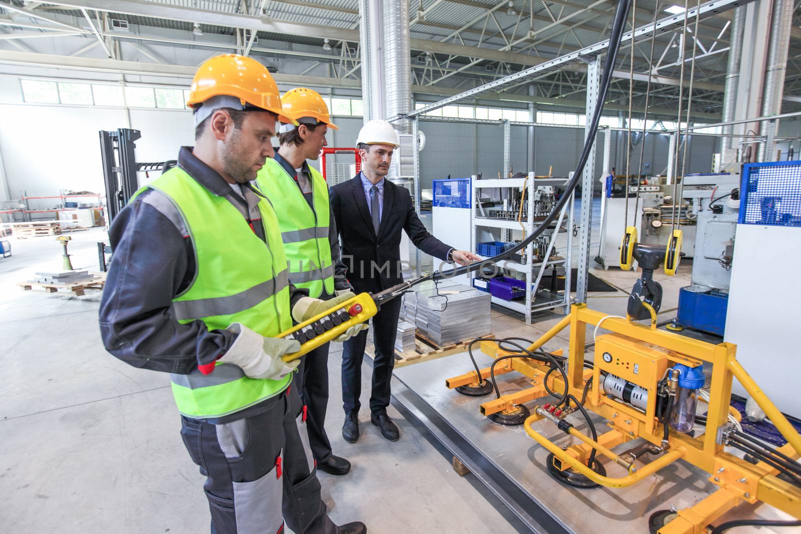Manager and workers working with metal sheet lifting device at CNC factory