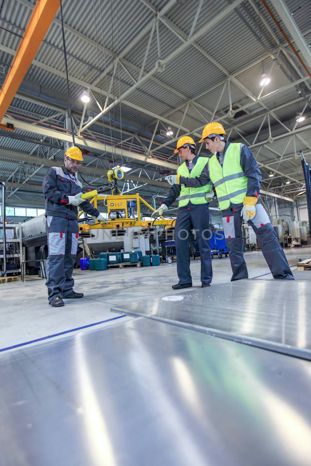 Manager and workers working with metal sheet lifting device at CNC factory