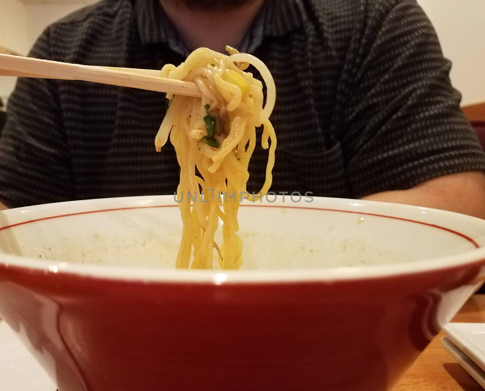 man eating asian noodles in a red bowl with chopsticks