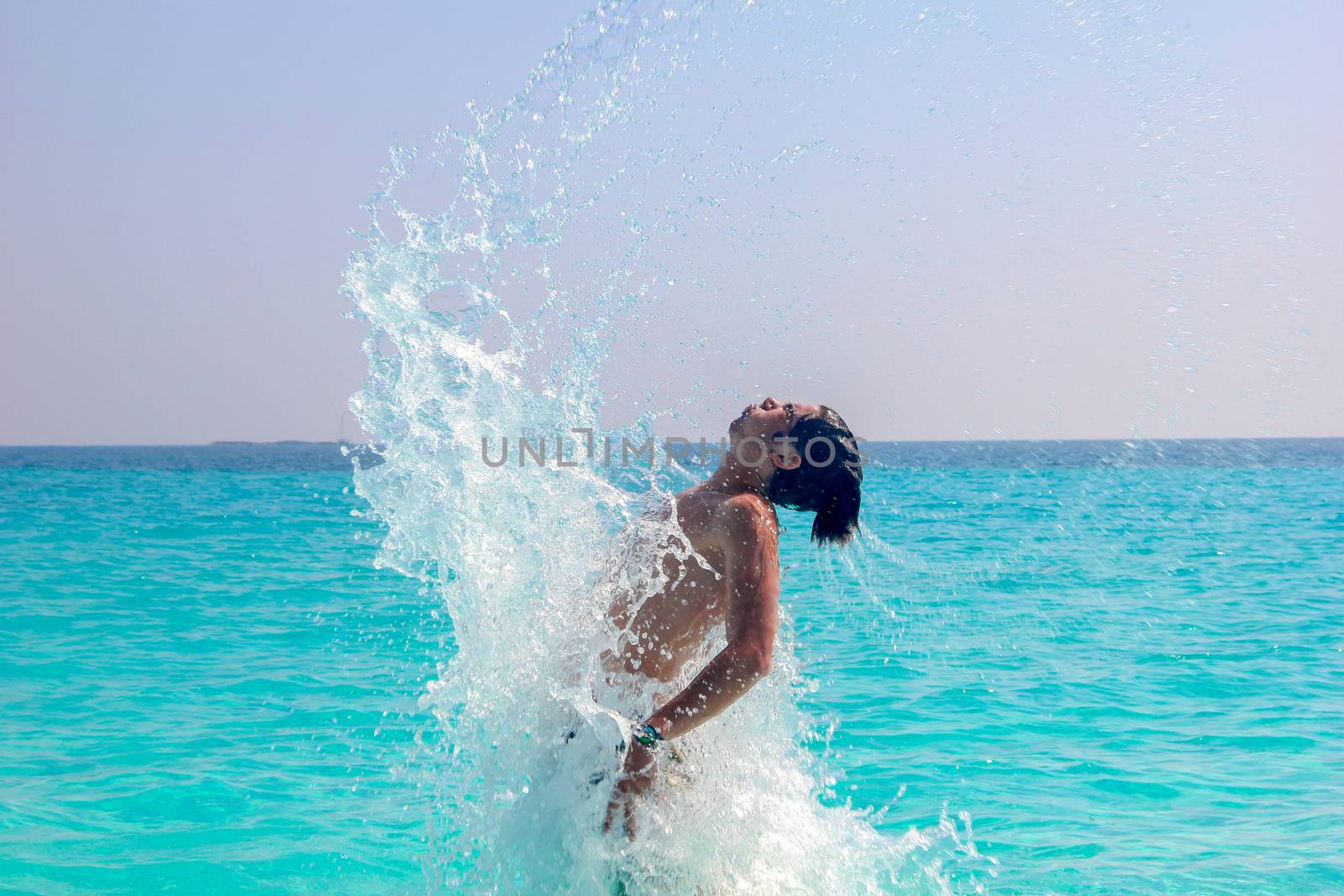 Man splashing water during summer holidays - Young attractive man having fun on a tropical beach at sunset