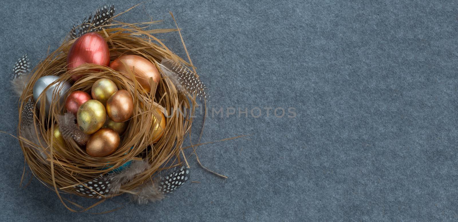 Happy Easter holiday greeting symbol stylish natural wooden grass nest with colorful quail eggs and feathers on gray fabric background