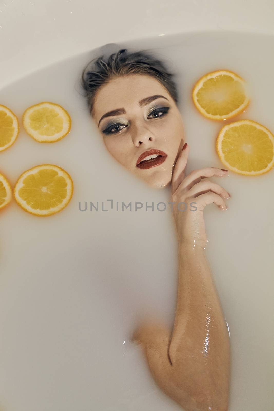 Young woman in the bath of milk and with oranges slices. Conceptual fashion photography for design. Skin care and a healthy lifestyle. Closeup naked young woman. Young woman for lifestyle design.