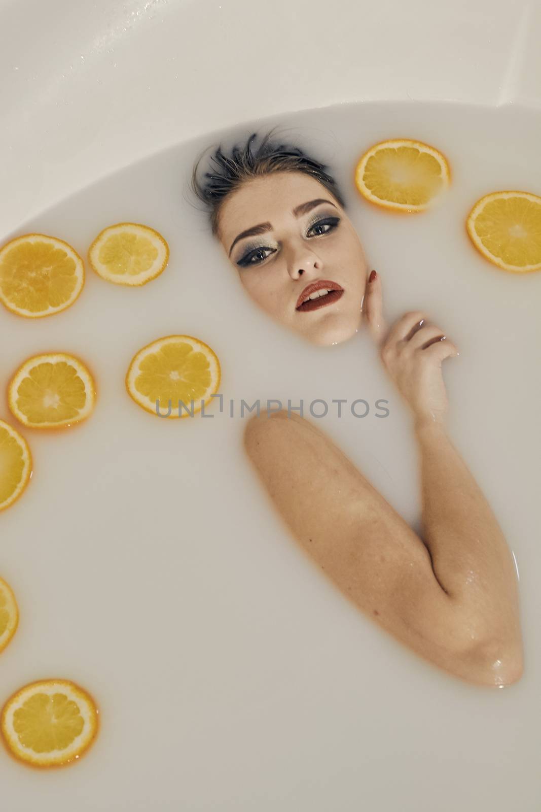 Young woman in the bath of milk and with oranges slices. Conceptual fashion photography for design. Skin care and a healthy lifestyle. Closeup naked young woman. Young woman for lifestyle design.