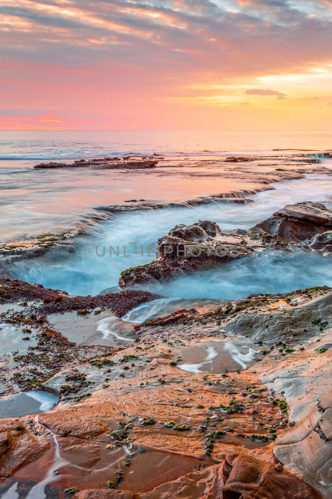Ocean tide flowing into coastal channels eroded over time, the beautiful sunrise casting warm light into the sky and rock shelf