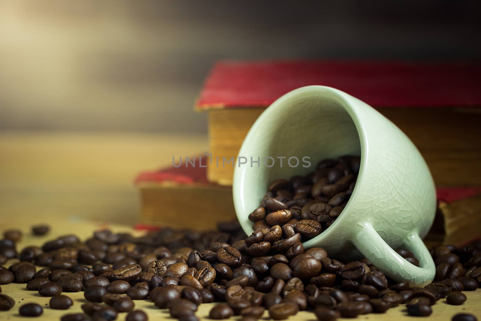 Coffee bean in tilted ceramic cup and old book laid behind on wooden table with morning light.