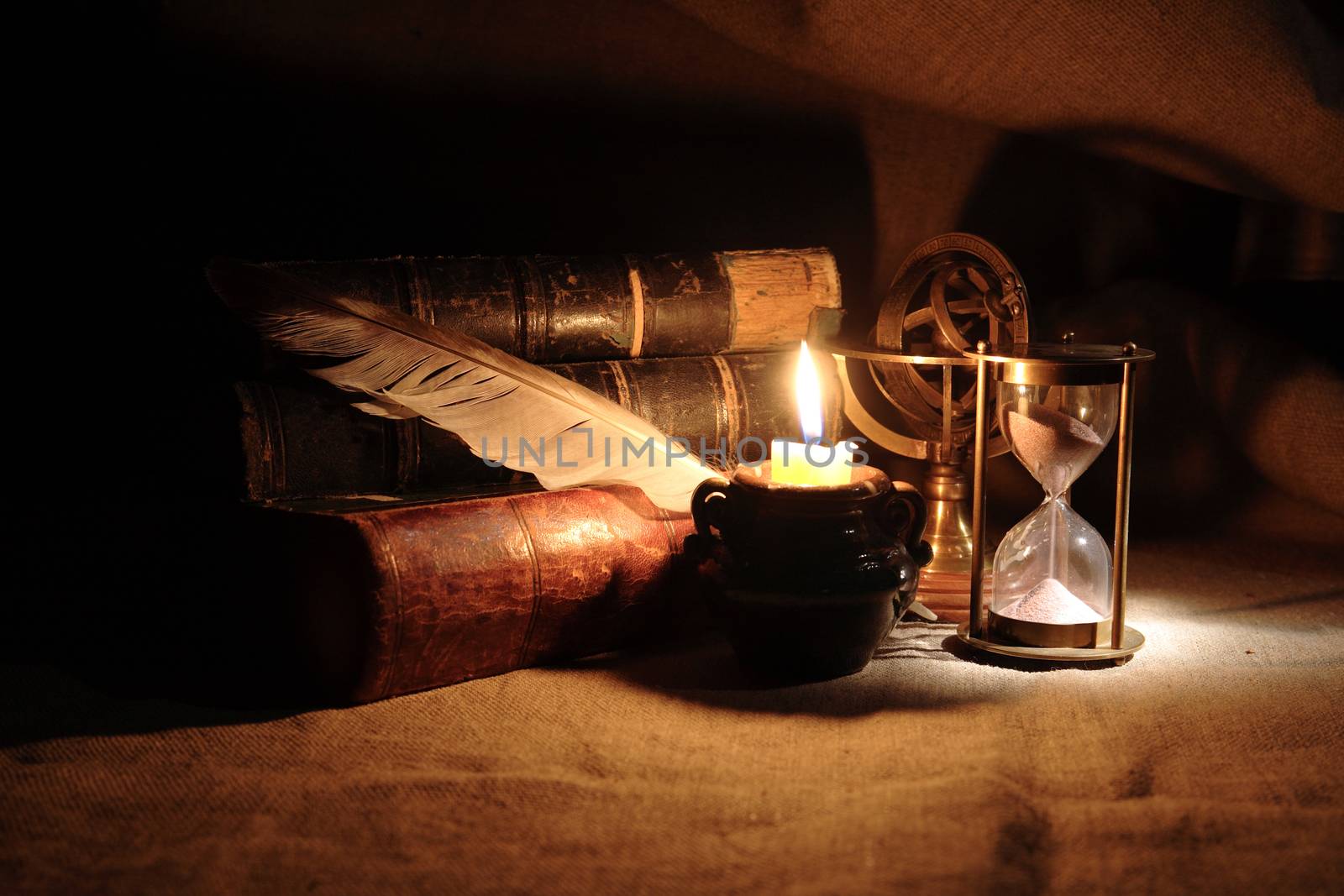 Vintage still life with hourglass near lighting candle and books