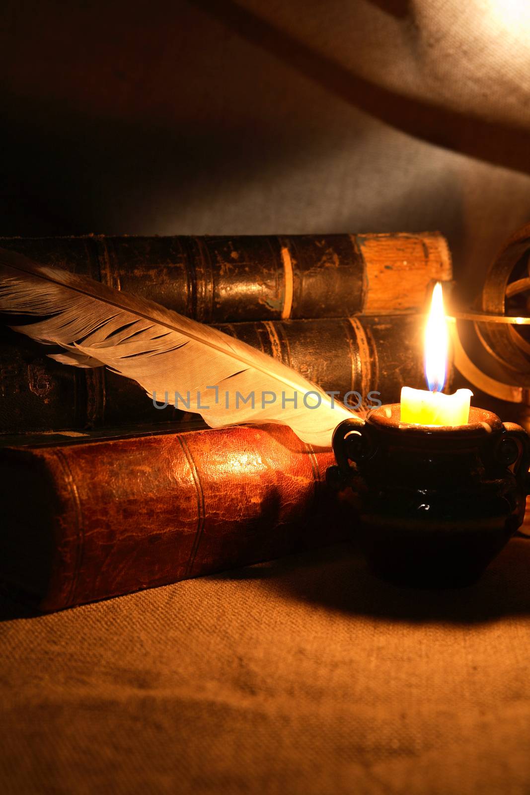 Vintage still life with quill pen near lighting candle and books