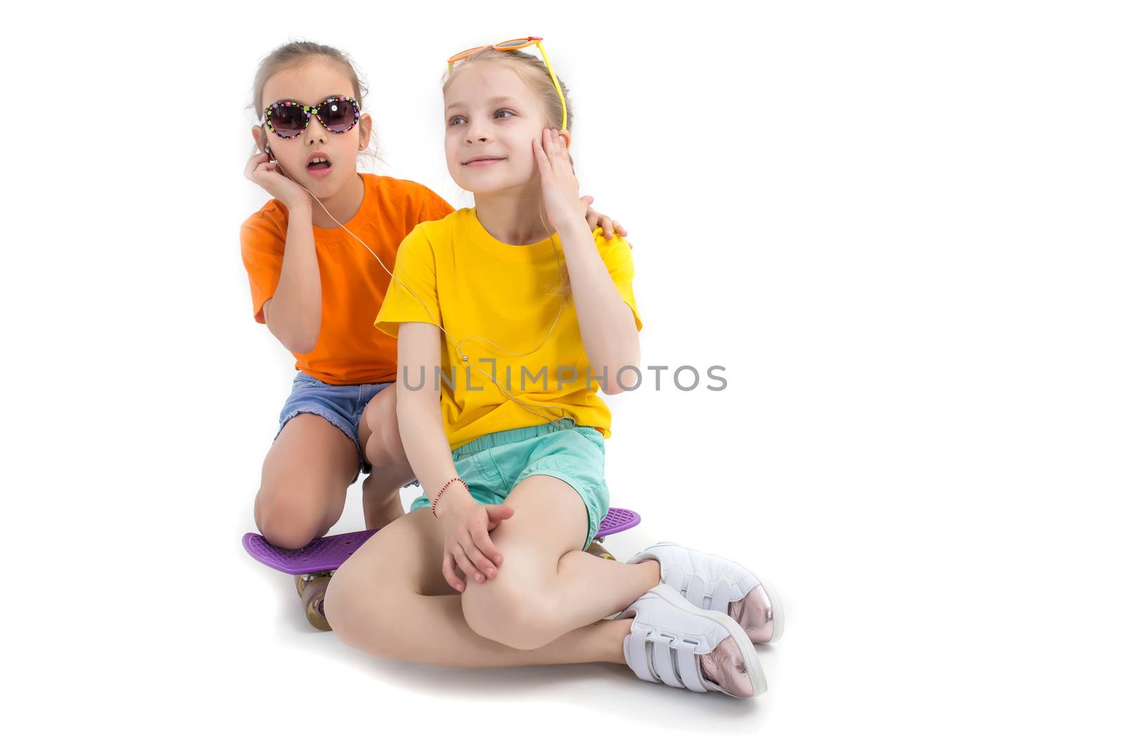 Two teen girls listenning to the music and sitting on skateboard over white