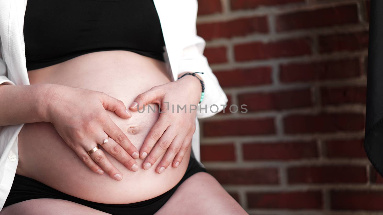 Pregnant Woman holding her hands in a heart shape on her baby bump by natali_brill