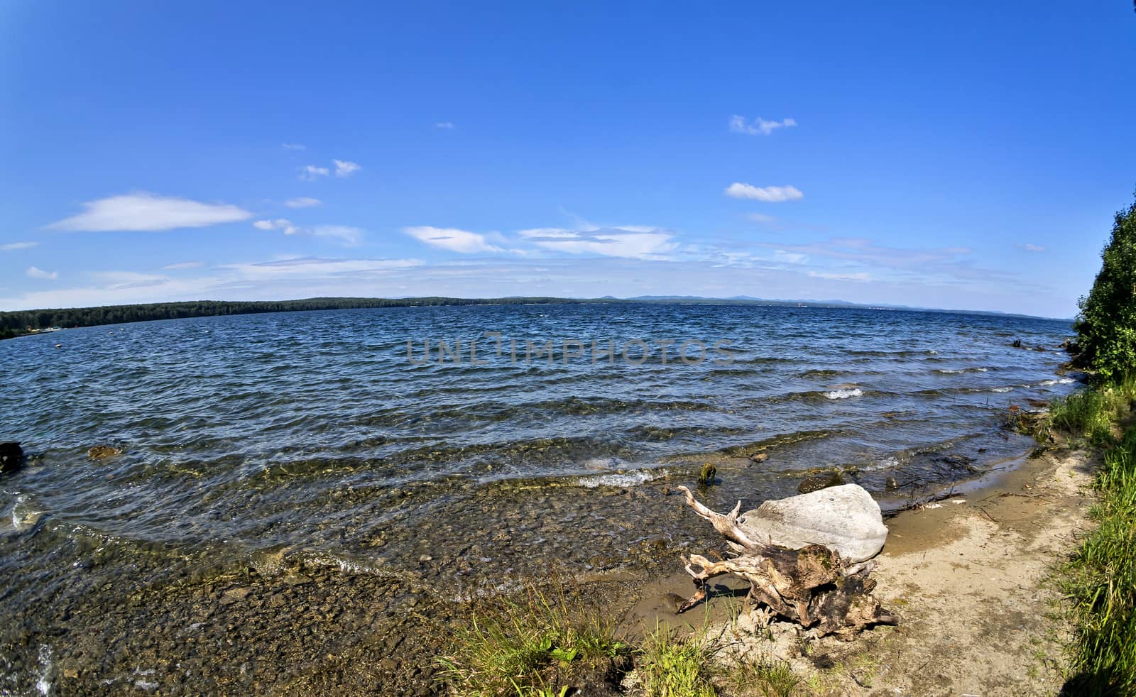 wooded and rocky shore on the background of the lake and the blue sky, fish-eye