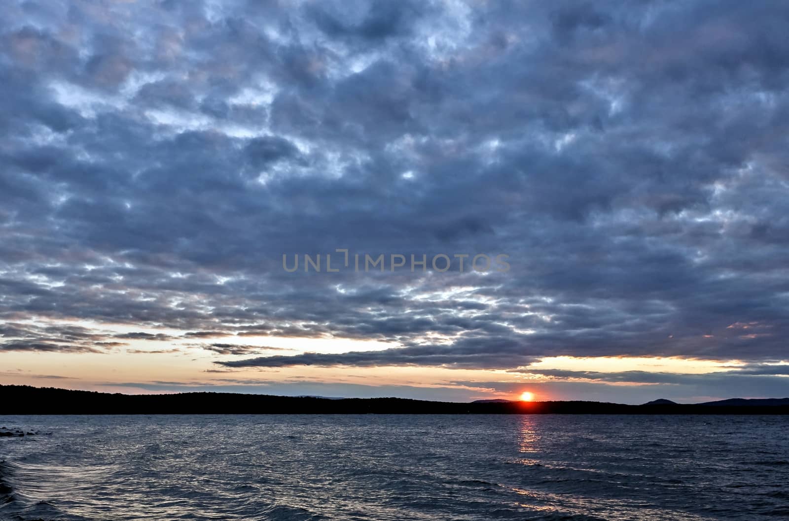 the evening sky over the lake, silhouettes of clouds illuminated by the sun