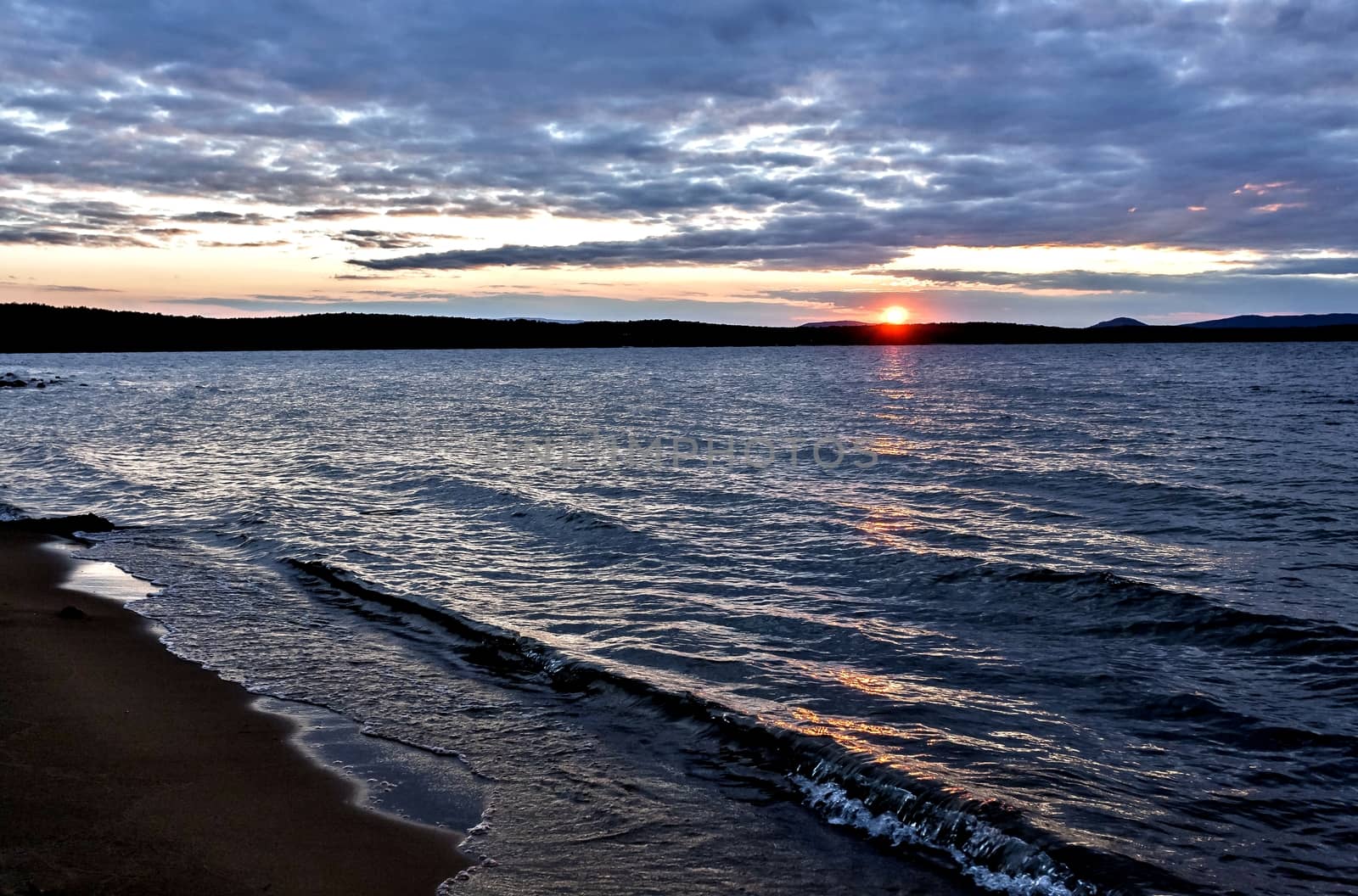 the evening sky over the lake, silhouettes of clouds illuminated by the sun